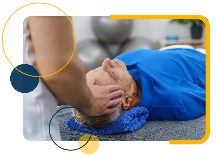 Therapist performing head and neck massage on elderly man lying on massage table with blue towel.
