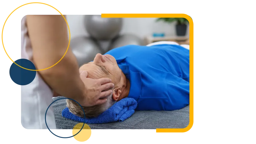 Therapist performing a head massage on an elderly man lying on a massage table with a blue towel under his head.