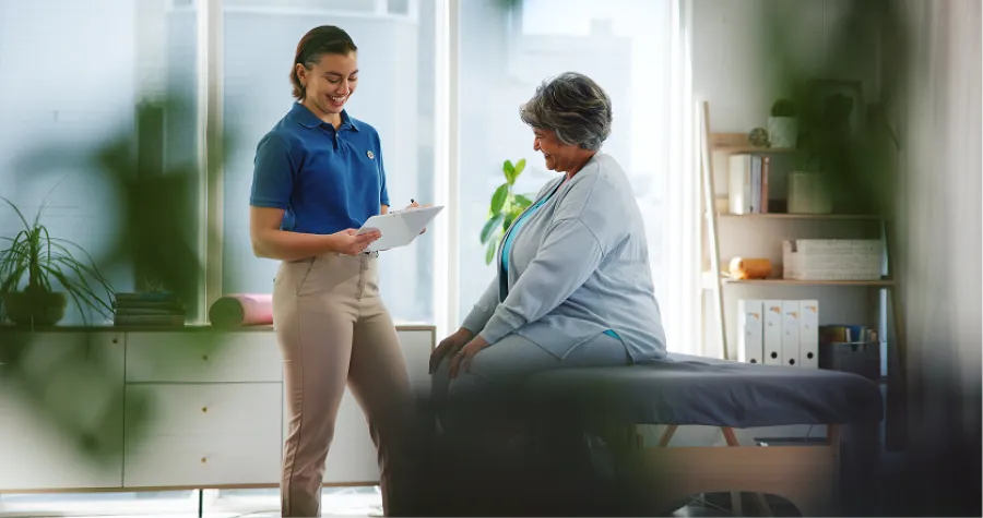 Young healthcare professional discussing treatment plan with older woman sitting on medical exam table.