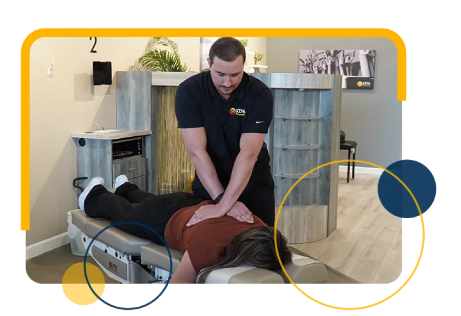 Chiropractor performing back adjustment on patient lying face down on treatment table in clinic.