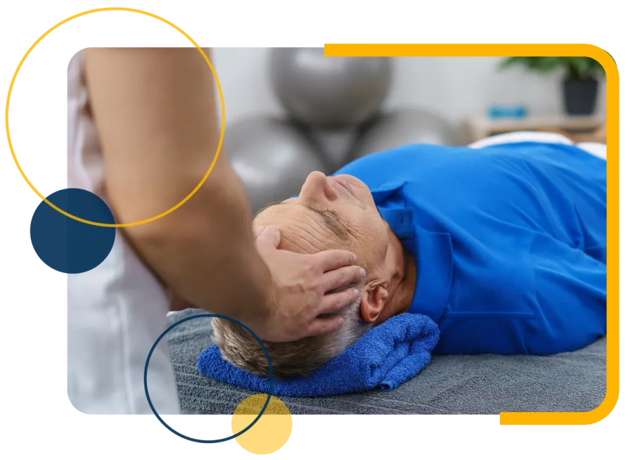Therapist performing head massage on elderly man lying on a massage table with blue towel under head.