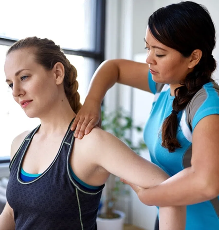 Female physiotherapist assisting woman with shoulder stretch in bright clinic setting.