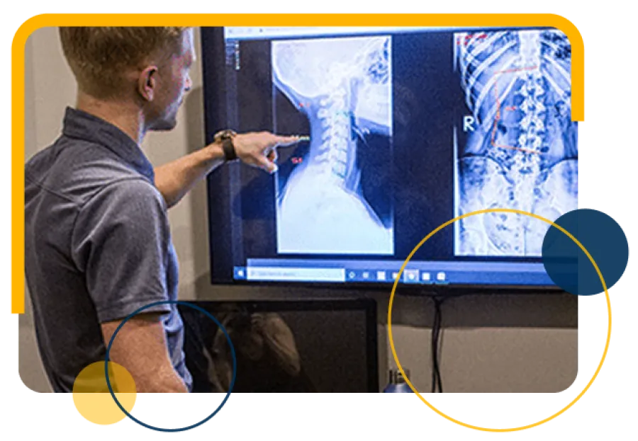 Man examining spinal X-ray images on a large screen in a medical office or clinic setting.