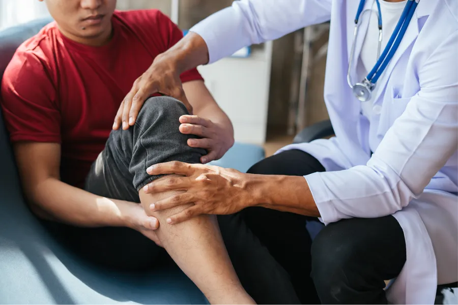 Doctor examining patient's knee during a medical consultation in a clinic setting.