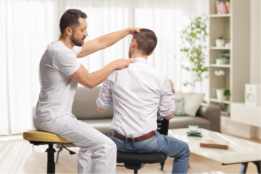 Chiropractor adjusting patient's neck and shoulders in a bright, modern living room setting.