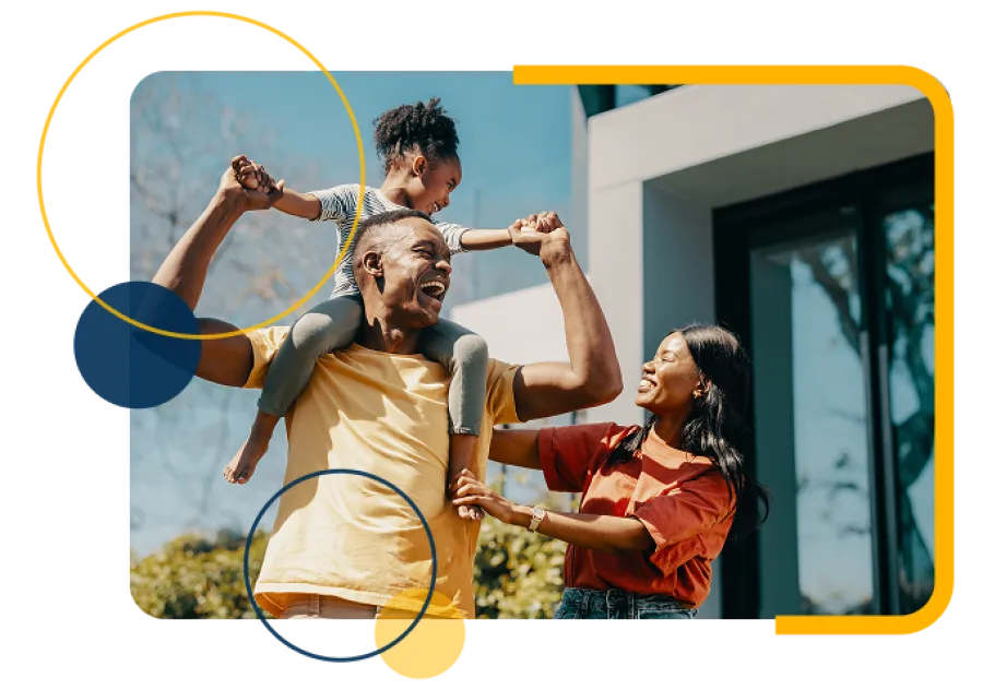 Happy family outdoors with father carrying daughter on shoulders and mother smiling beside them near modern house.
