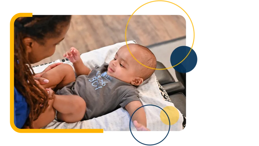 Mother playing and bonding with her infant son lying on a blanket indoors by wooden floor.