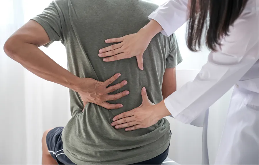 Doctor examining a man's lower back pain during a medical consultation in a bright clinic room