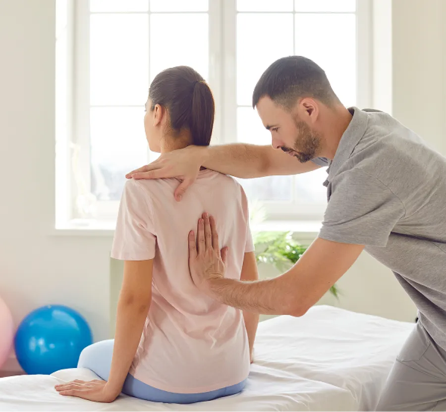 Physical therapist adjusting a woman's posture during a rehabilitation session in a bright therapy room.