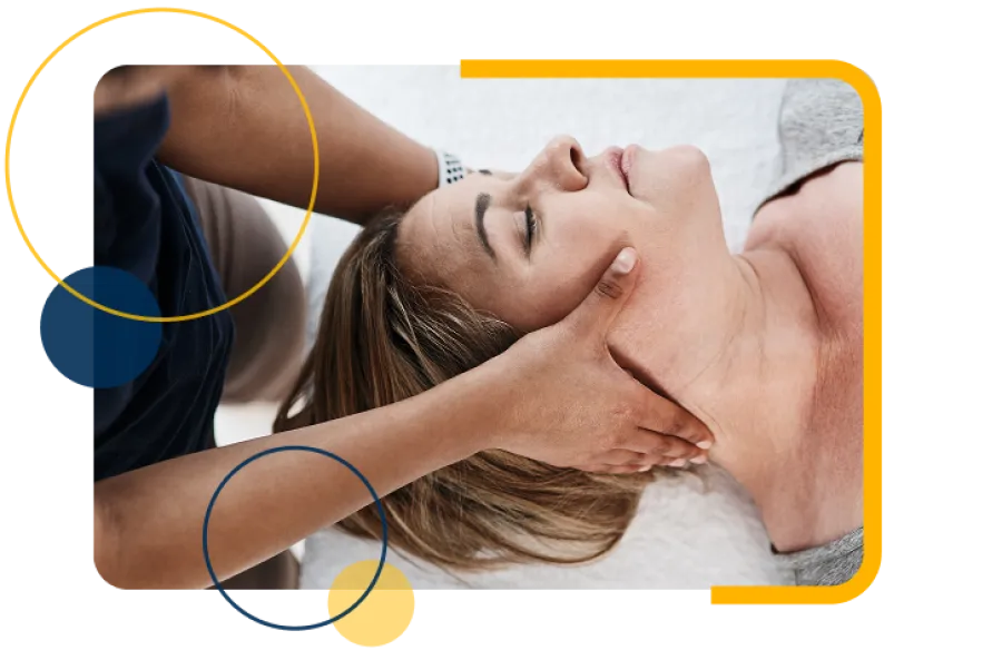 Therapist giving a relaxing head and neck massage to a woman lying with closed eyes on a white bed.