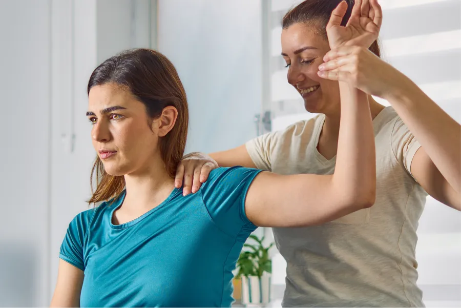 Physical therapist assisting woman with shoulder exercises during rehabilitation session indoors