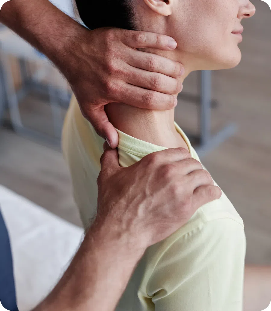 Therapist performing neck and shoulder massage on a patient wearing a light yellow shirt indoors.