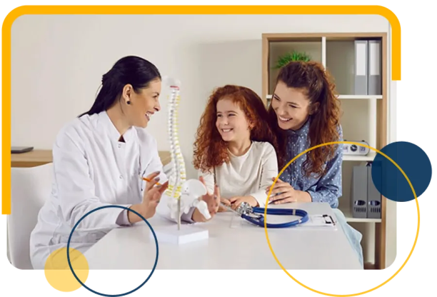 Doctor explains spine model to smiling mother and daughter in bright medical office consultation.