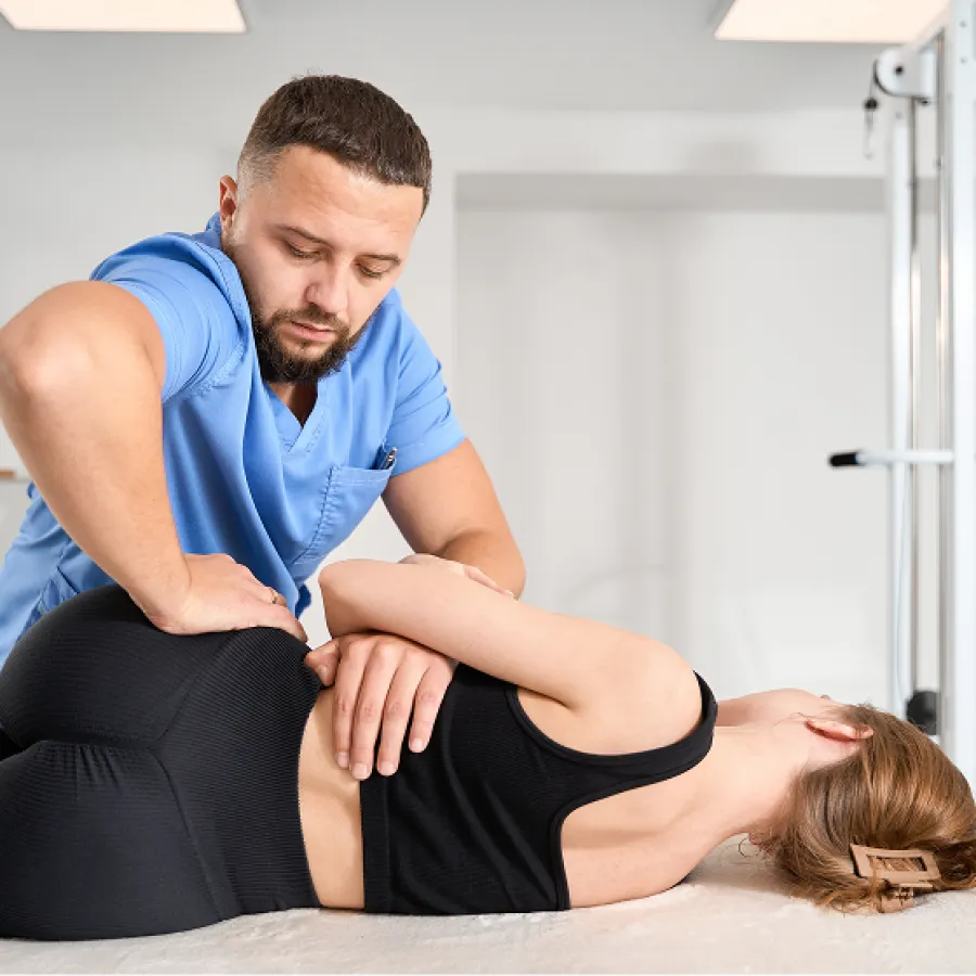 Physical therapist in blue scrubs performing manual therapy on a woman lying on a treatment table.