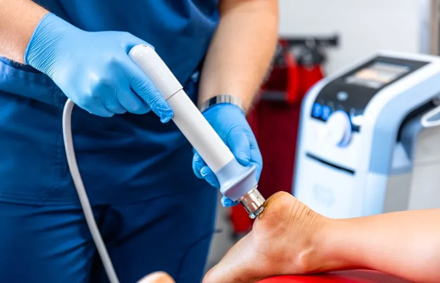 Medical professional performing laser therapy treatment on a patient's heel in a clinical setting.