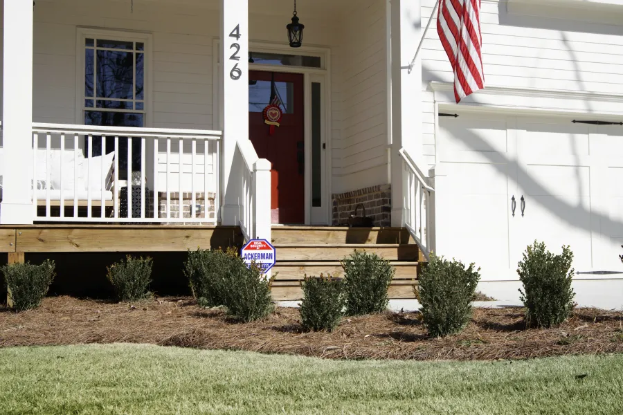 Front porch of white house with red door, American flag, with Ackerman sign