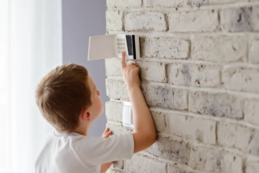 Young boy adjusting a digital thermostat on a white brick wall in a bright room