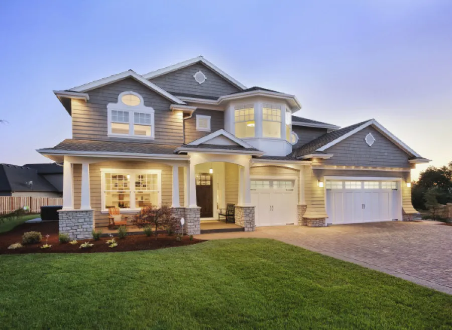 Spacious two-story modern house with illuminated porch, large windows, double garage, and manicured lawn at dusk