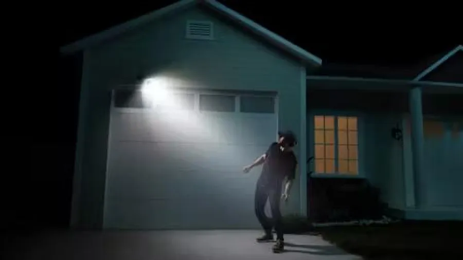 Thief illuminated by a bright outdoor light near a house garage at night creating dramatic shadows.