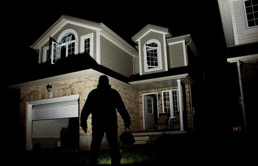 Silhouette of a thief holding a bag standing outside a house at night with porch light on