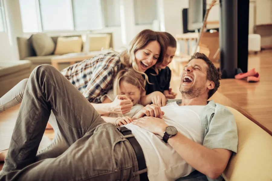 Joyful family playing together, laughing on the floor in a bright living room.