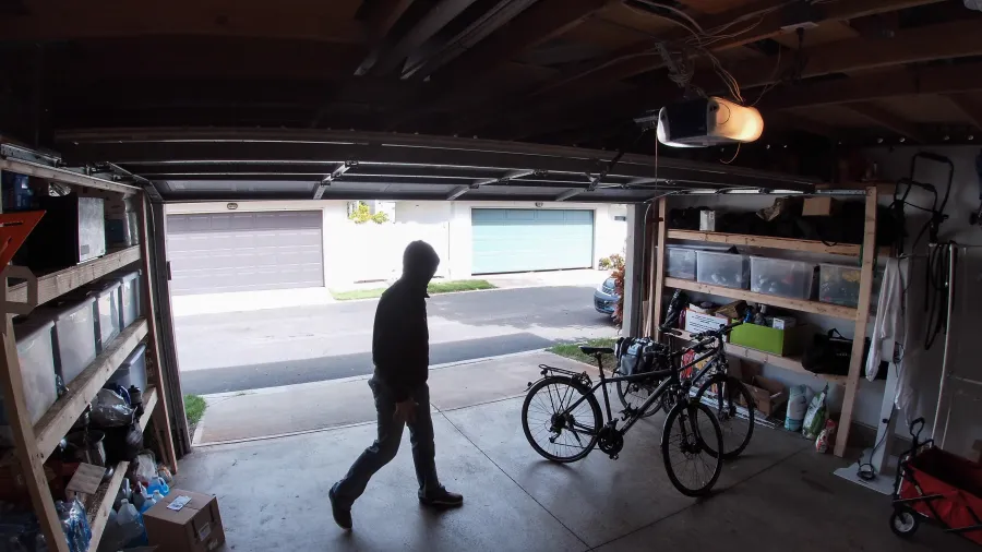 Person in dark hoodie walking inside a residential garage with two bicycles and storage shelves.