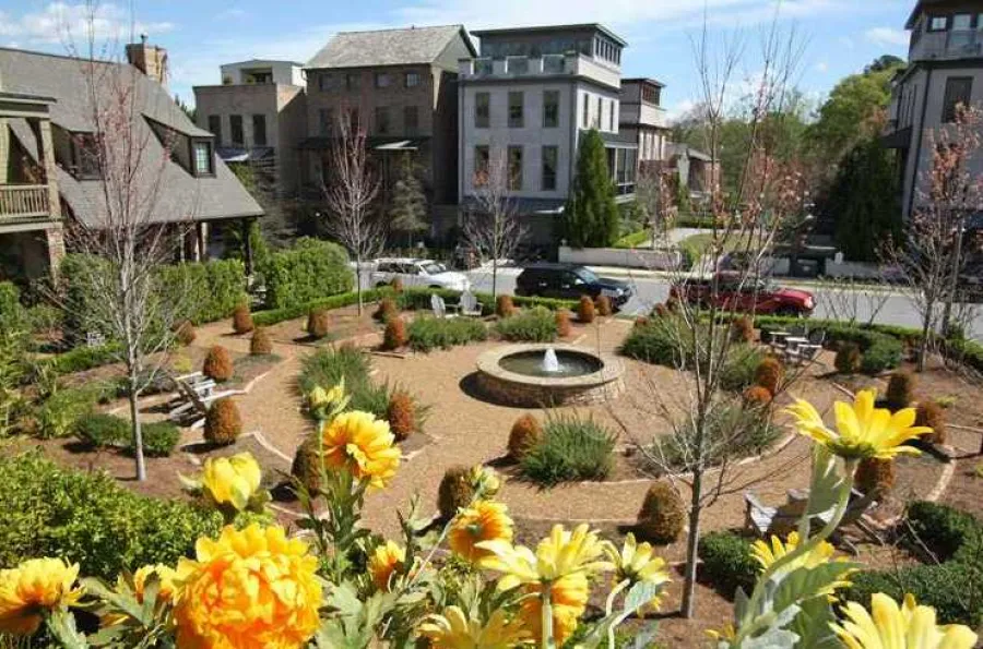 Woodstock community garden with yellow flowers, central fountain, and surrounding residential buildings on a sunny day