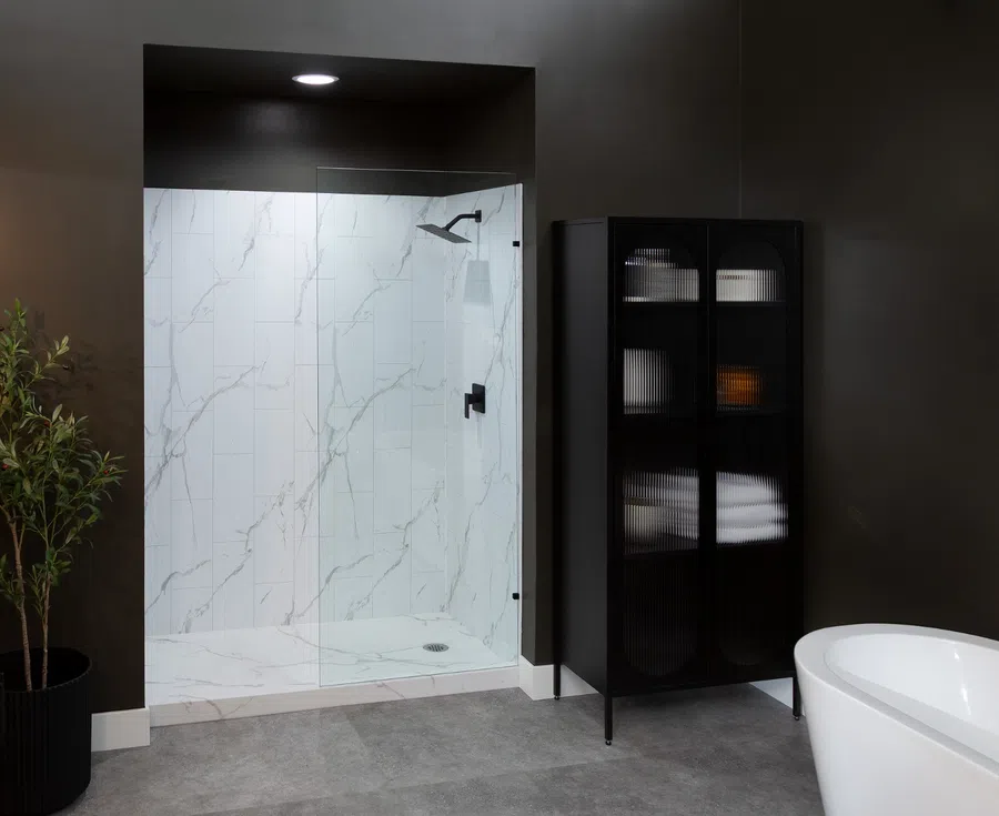 Modern bathroom with glass shower enclosure, marble tile walls, black storage cabinet, white bathtub, and dark walls.