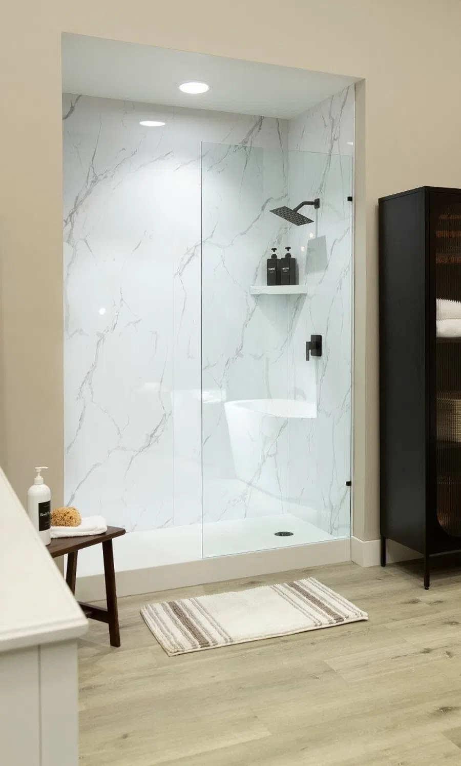 Modern bathroom with freestanding tub, glass shower, black storage cabinet, and wood flooring under warm lighting.