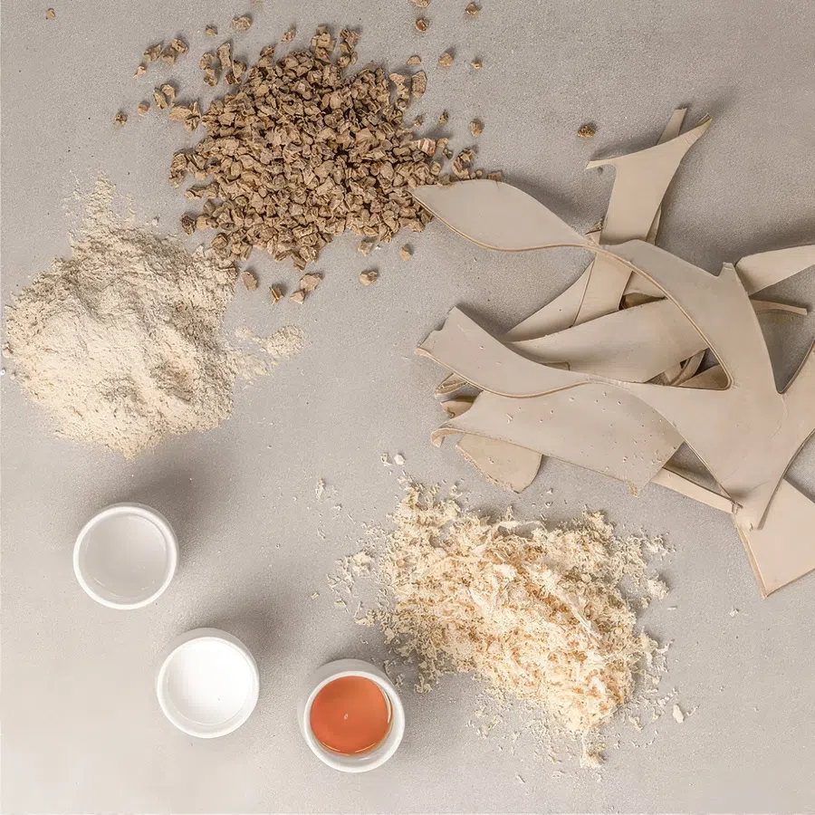 Various natural material samples including beige powder, wood shavings, chopped wood pieces, tan leather scraps, and small containers on gray surface.