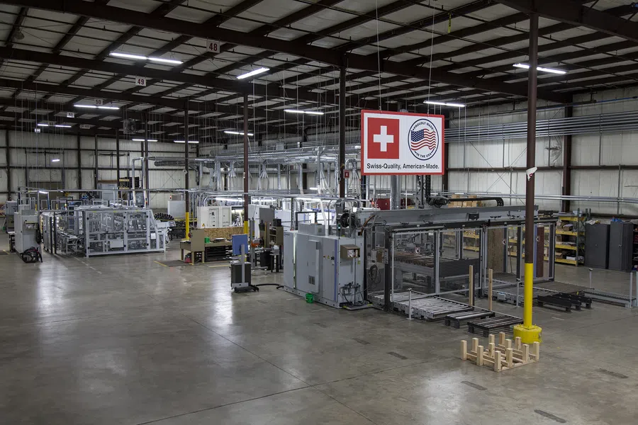 Spacious modern industrial factory floor with automated machinery and a sign showing Swiss and American flags.