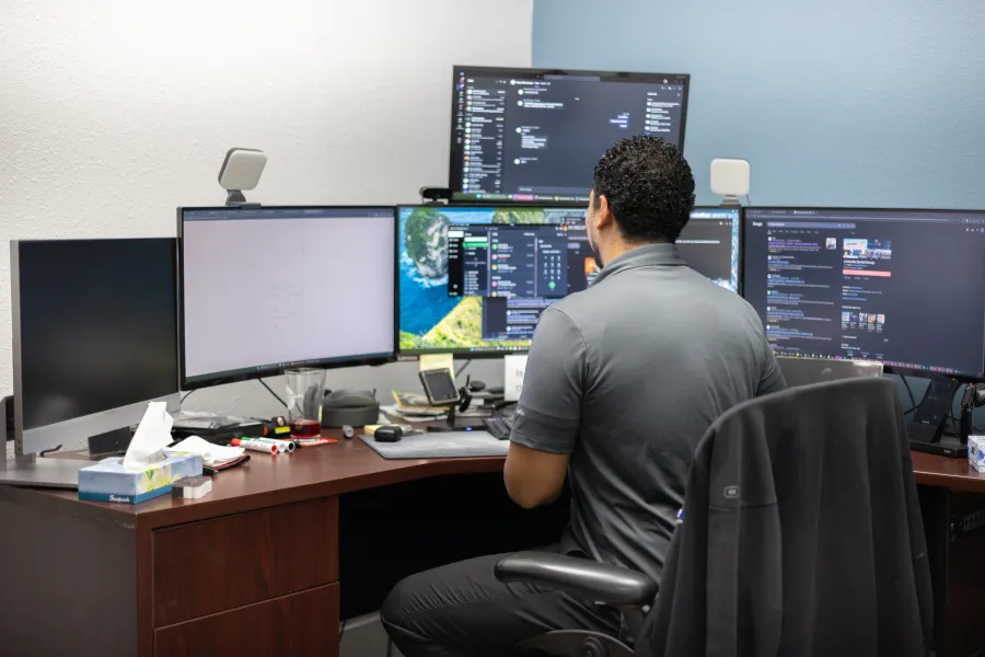 a man sitting at a desk with several monitors