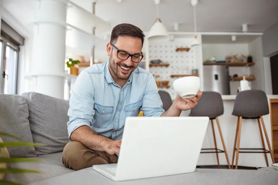 a man sitting on a couch with a laptop and a cup of coffee