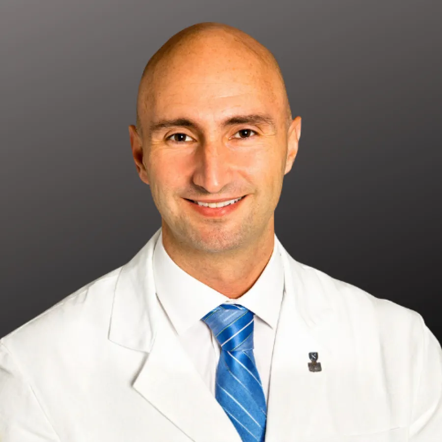 Smiling bald male doctor wearing white coat and blue striped tie against a gray background