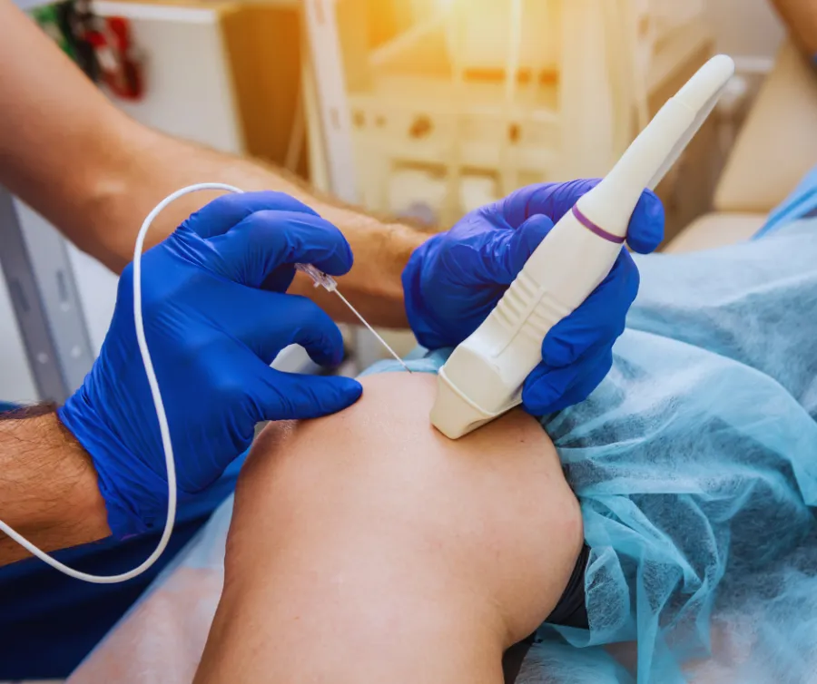 Doctor wearing blue gloves performs ultrasound-guided injection on patient's knee in medical clinic.