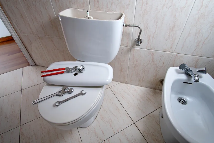 Toilet with removed tank lid and plumbing tools on toilet seat for bathroom repair or maintenance