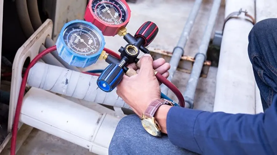 Technician holding HVAC manifold gauges testing and adjusting air conditioning system pressures.