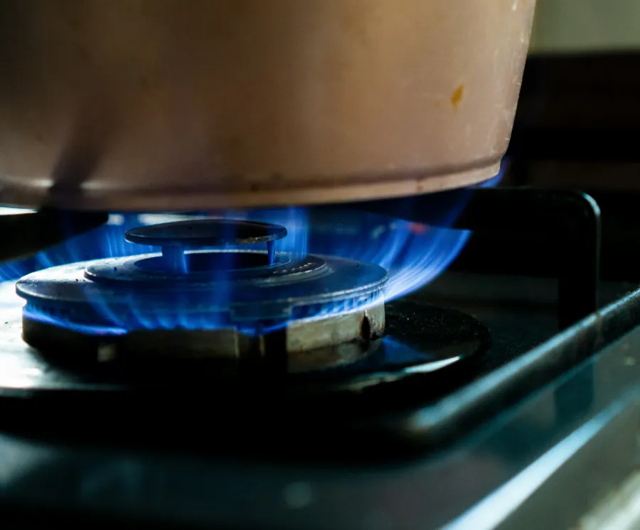 Blue gas flame heating a pot on a stovetop burner in close-up view of a kitchen setup.