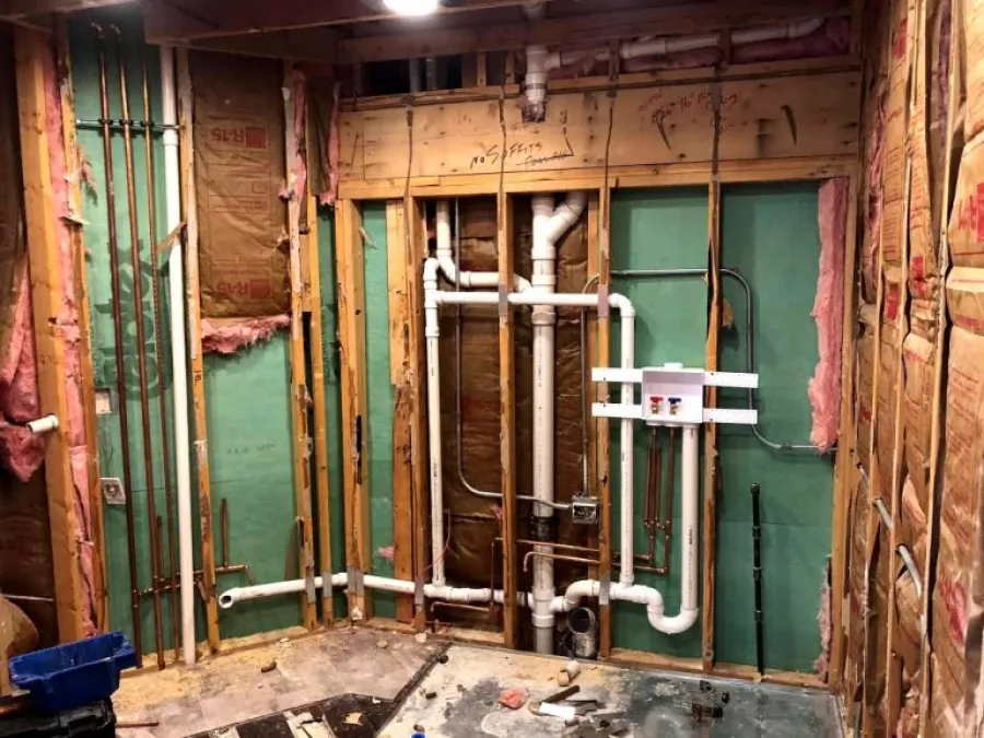 Construction site with trench dug for drainage pipe installation near a garage with white doors and trees.