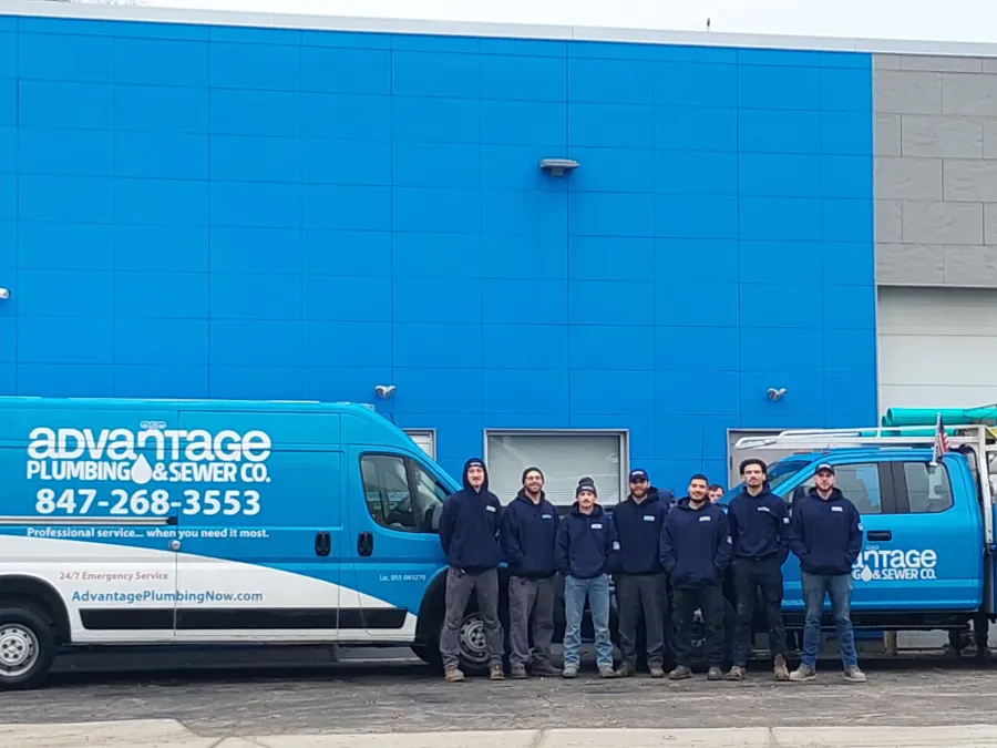 Advantage Plumbing & Sewer Co. team stands in front of company vans outside a building with a blue wall.