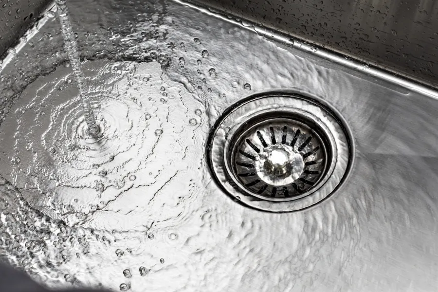 Stream of water flowing into a clean stainless steel kitchen sink with visible drain and rippling water.