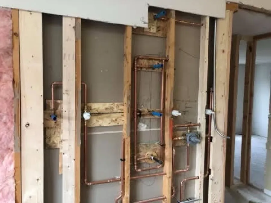Interior wall framing with exposed copper plumbing pipes and valves in a residential construction site.