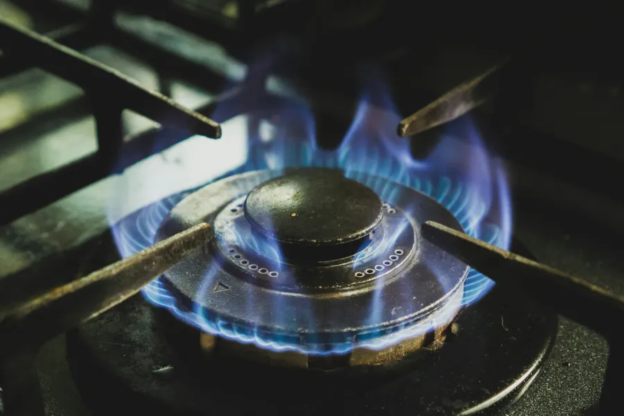 Close-up of a gas stove burner with blue flame lit on a black stovetop in a kitchen