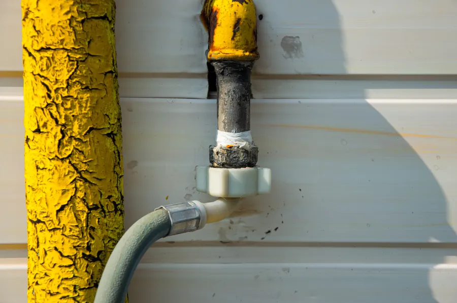 Close-up of a yellow, rusted pipe connected to an outdoor faucet with a green garden hose attached.
