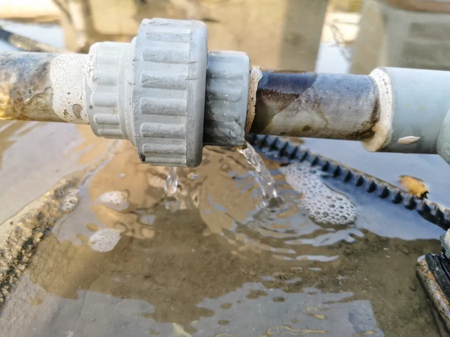 Close-up of a leaking pipe joint with water dripping into a puddle below outdoors.