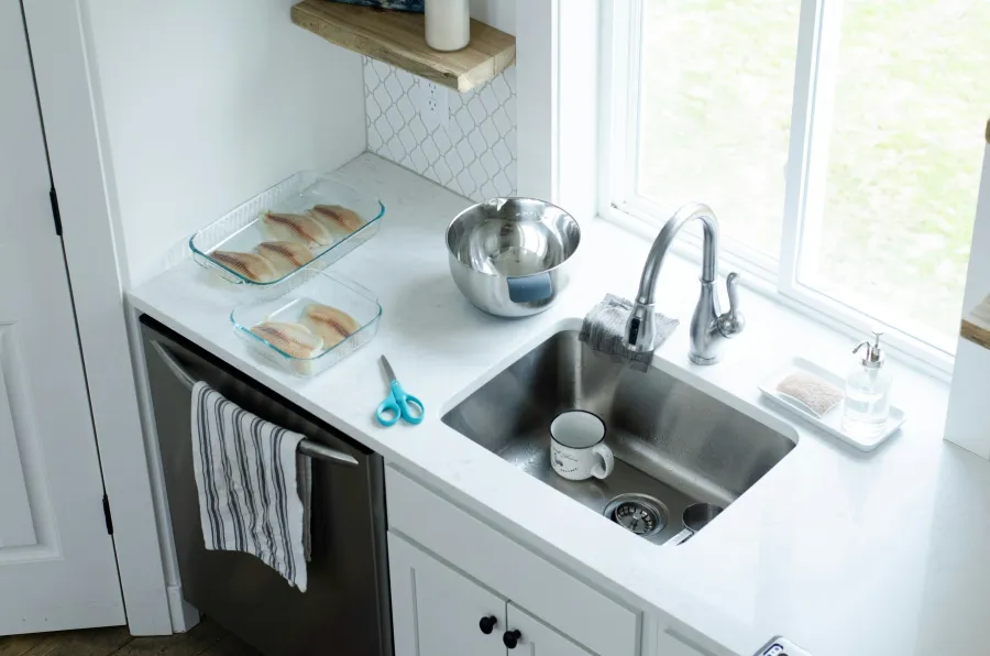 Clean kitchen countertop with prepared fish fillets, stainless steel bowl, sink, striped towel, and scissors.