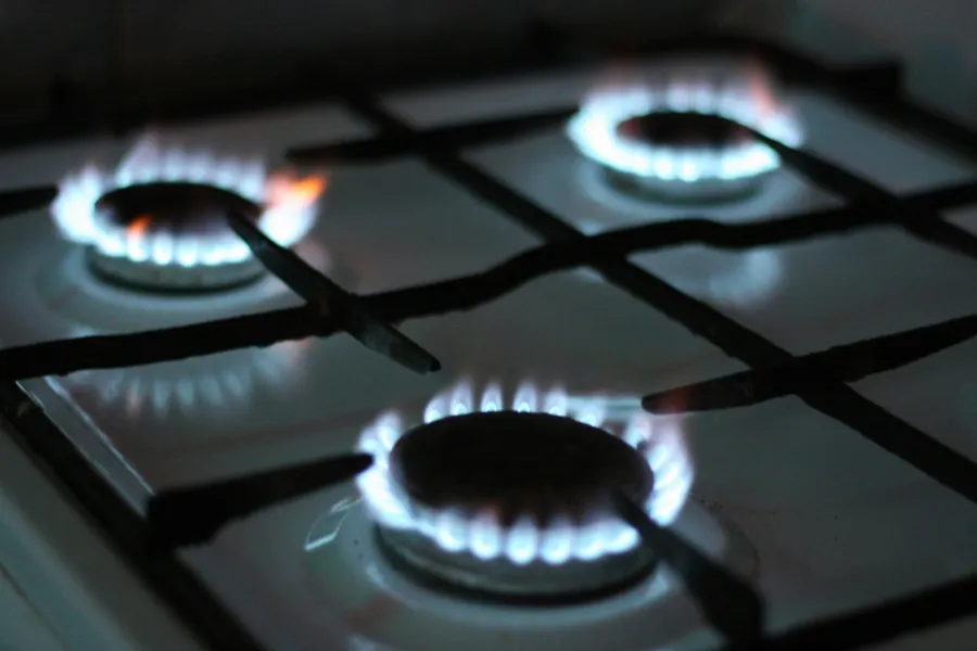 Close-up of a gas stove with three burners lit by blue flames in a dim kitchen setting.