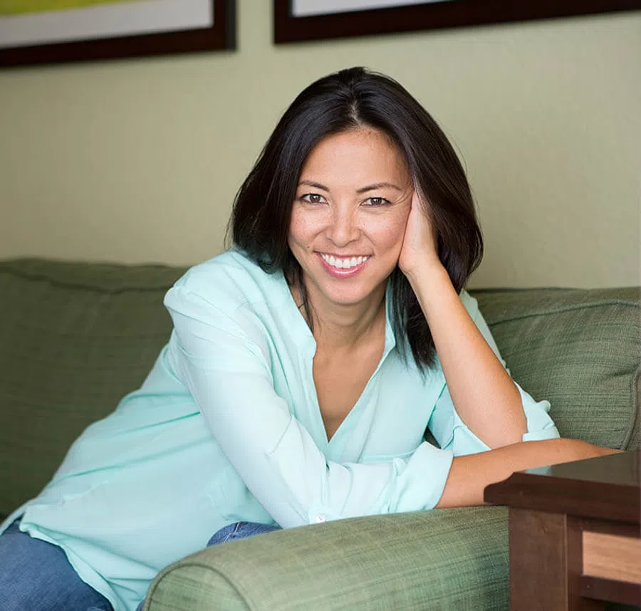 Smiling woman in a light blue shirt relaxing on a green couch with hand resting on her head