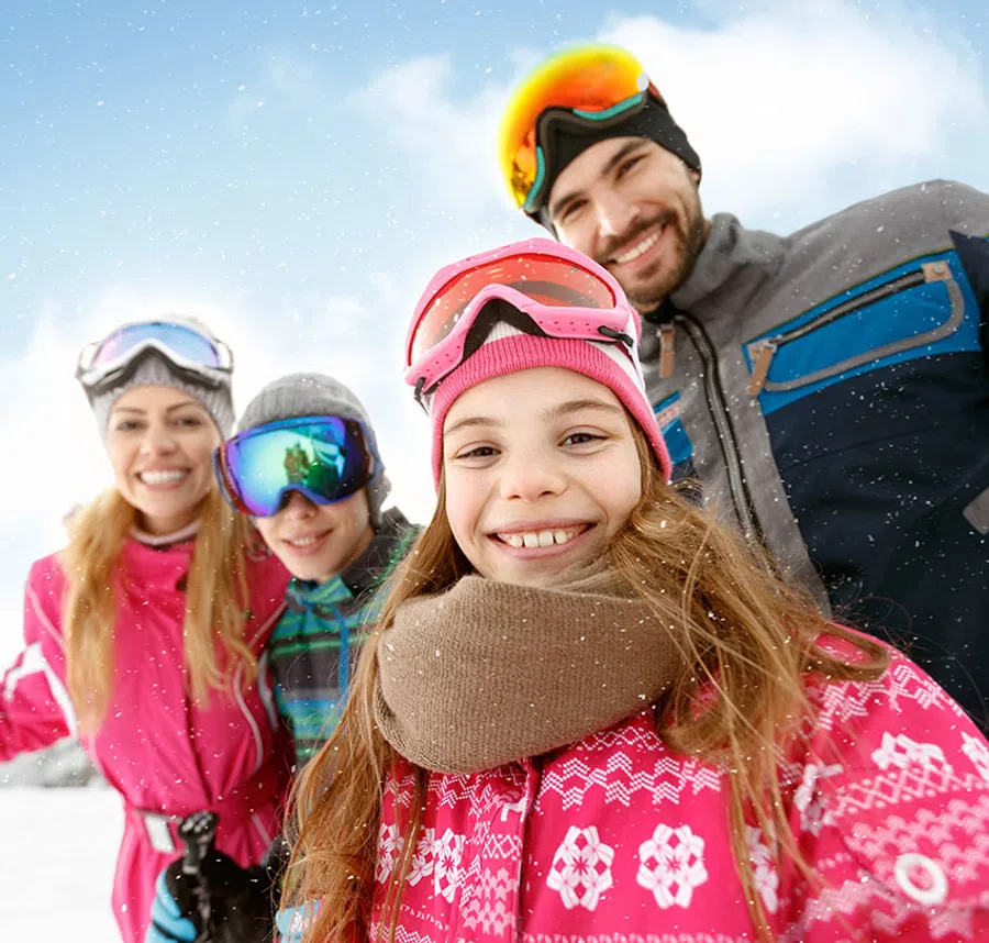 Happy family dressed in colorful winter gear enjoys snowy day outdoors smiling at camera.