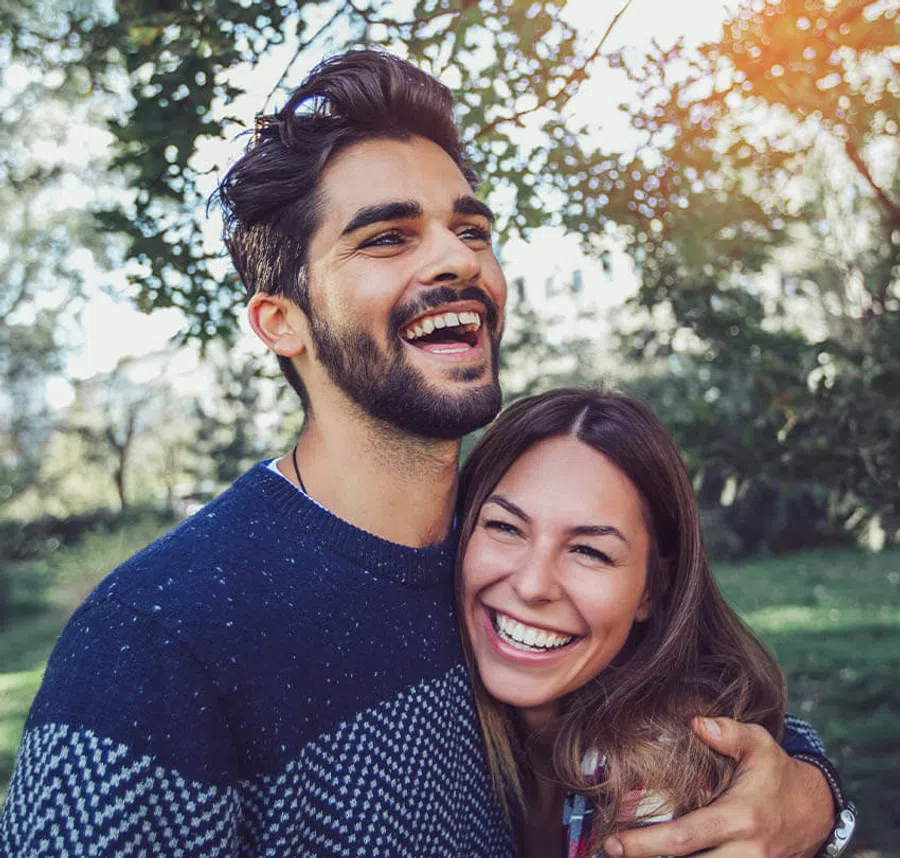 Young happy couple smiling and hugging outdoors in a sunny park with trees in the background
